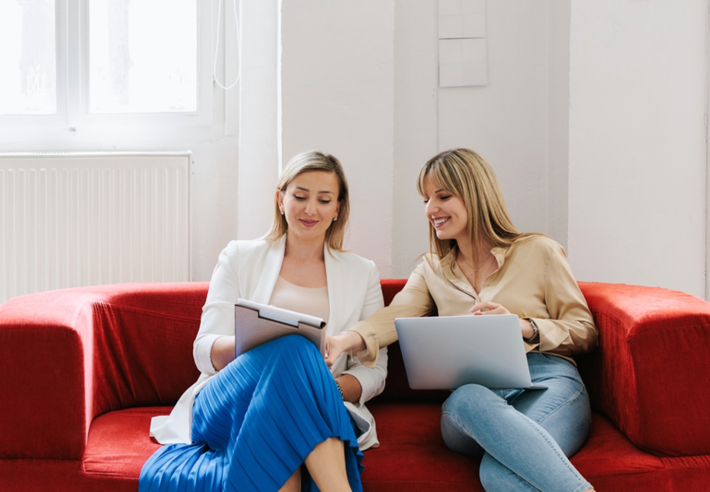 Two female colleagues sitting on an office couch talking